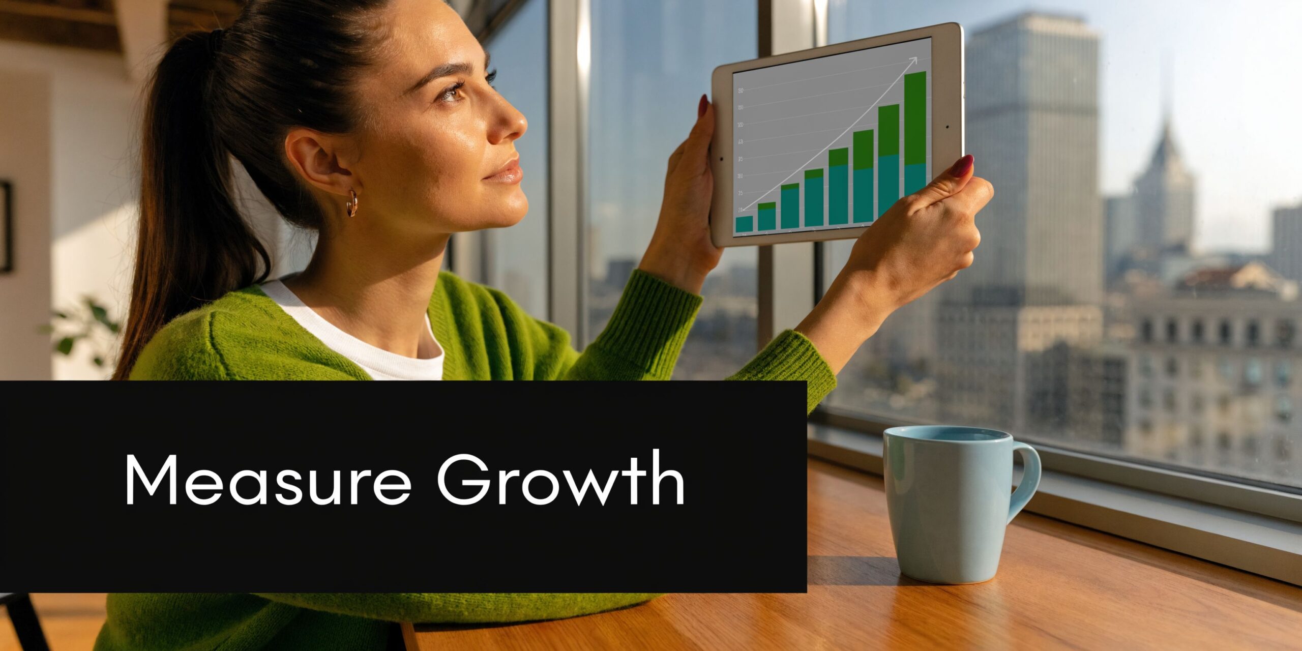 A professional woman in a green sweater examines a tablet displaying rising business growth charts.